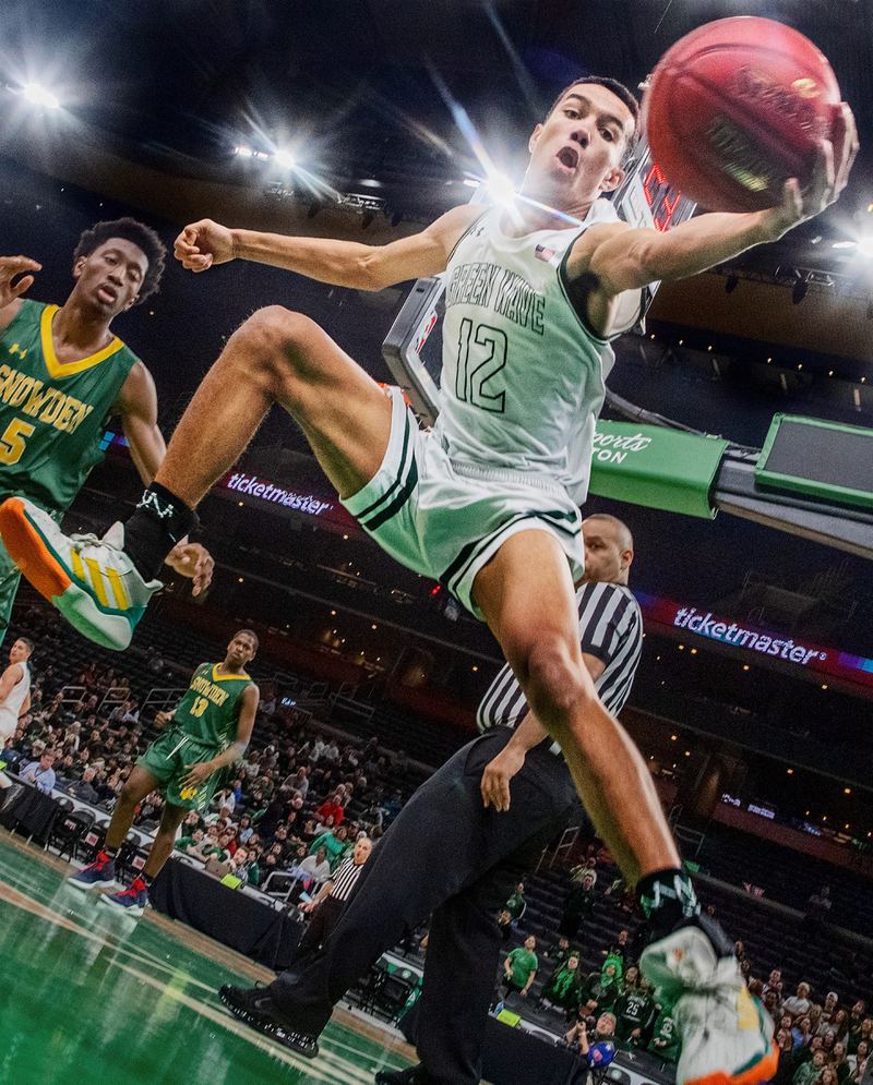 Shot from the floor under the basket, a player in a white number 12 jersey leaps for the ball as an official looks on