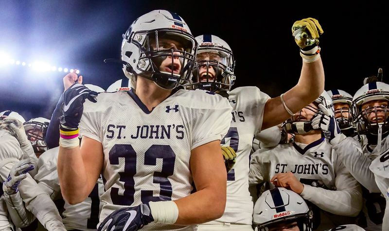 A football player in a number 33 jersey yells with his teammates crowded behind him under the lights