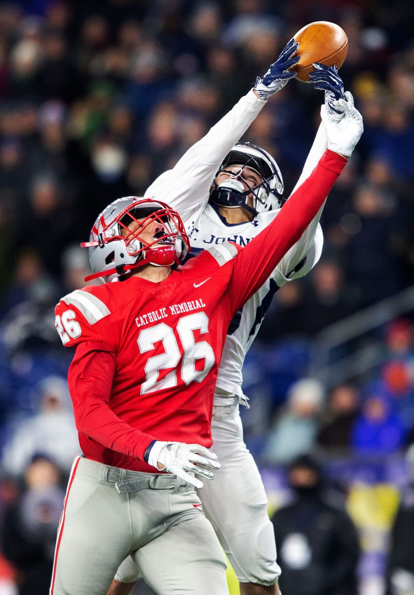 A St. John's receiver reaches over a Catholic Memorial defender in a red number 26 jersey for the ball