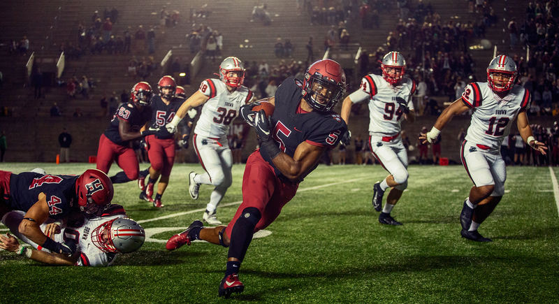 A running back breaks a tackle and turns upfield at a night game