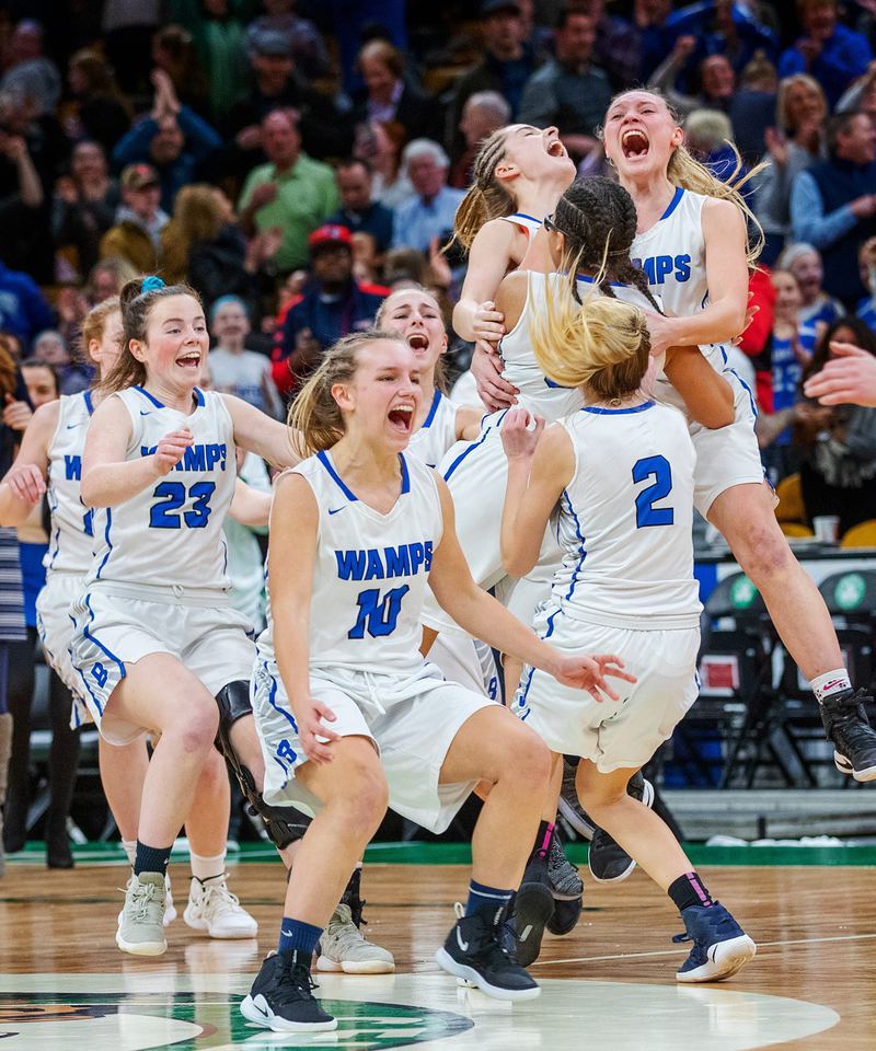 A girls basketball team in white jerseys screams and leaps into each other's arms at center court
