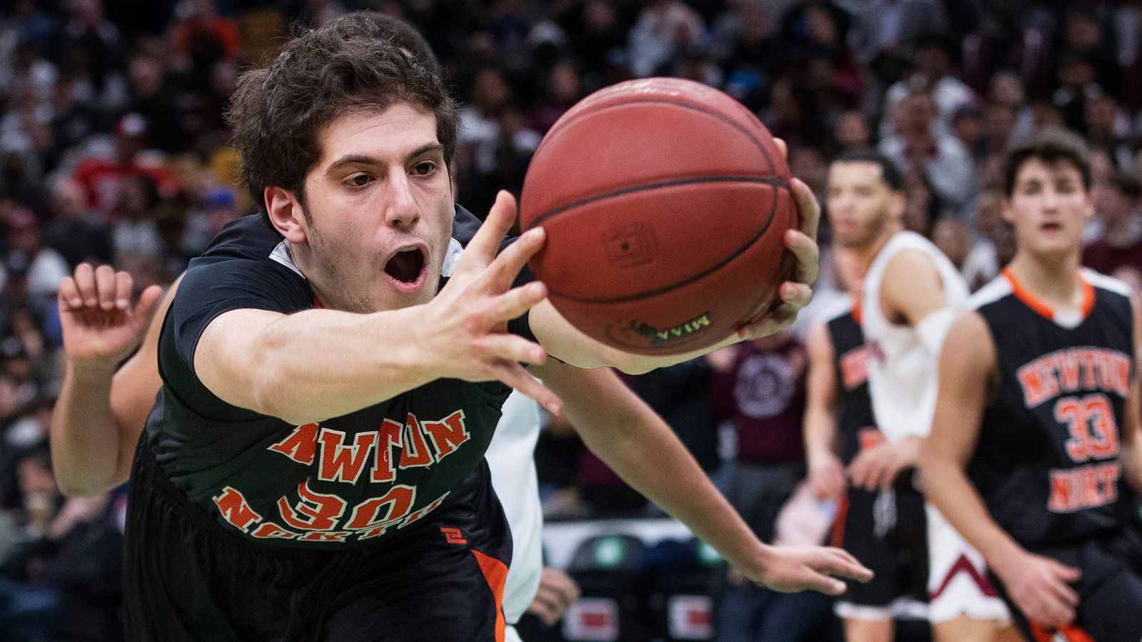 A basketball player in an orange number 30 jersey stretches the ball toward the hoop on a drive