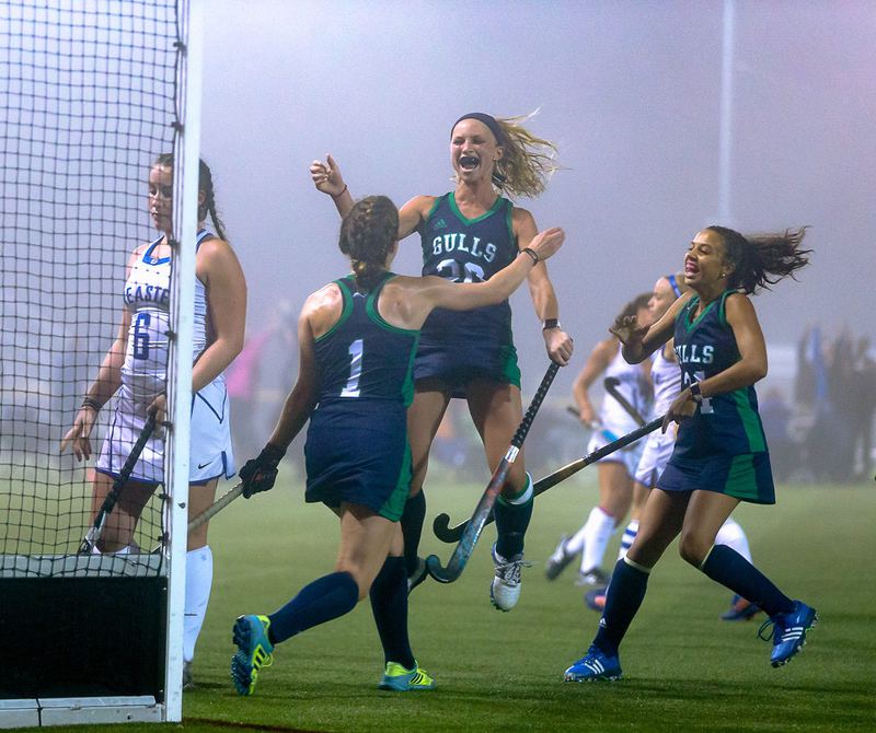 Field hockey players leap and run in to celebrate a goal on a foggy night