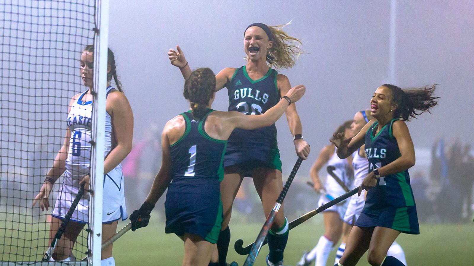 Field hockey players leap and celebrate a goal on a foggy night