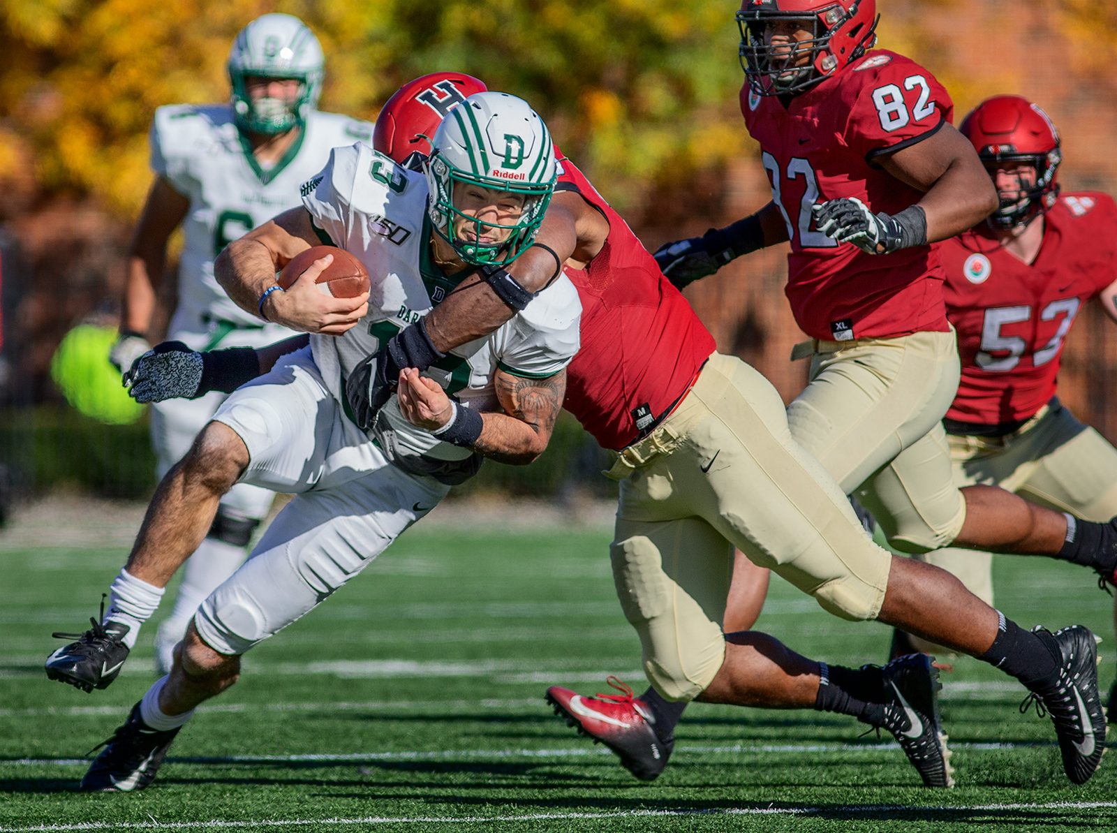 A Dartmouth running back in white lowers his head and drives through a Harvard tackler