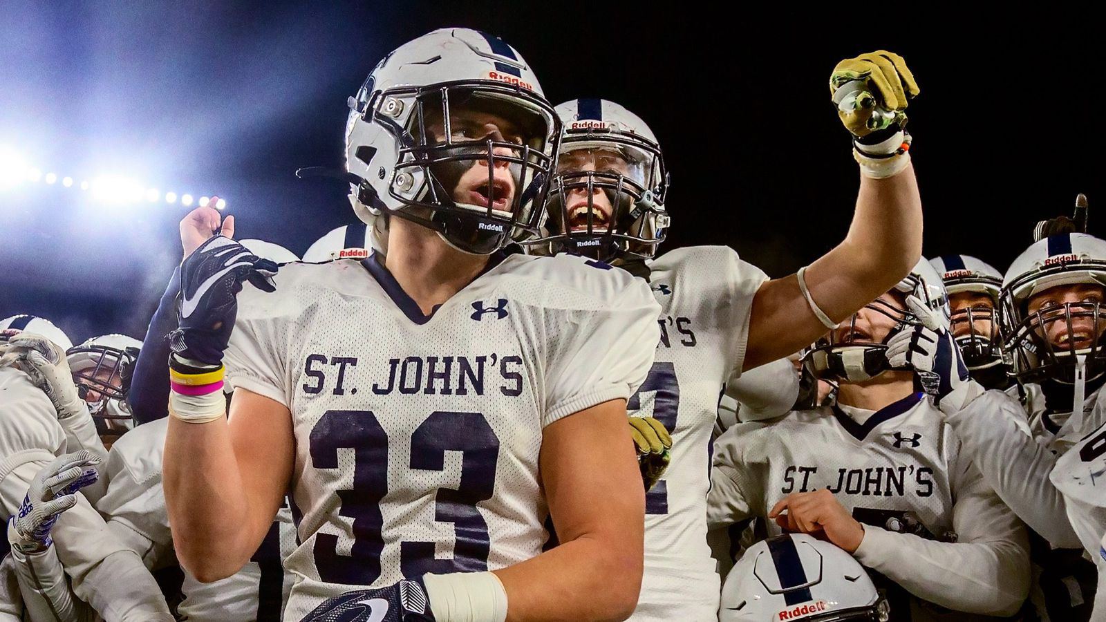 A football player in a number 33 jersey yells with his teammates under the lights
